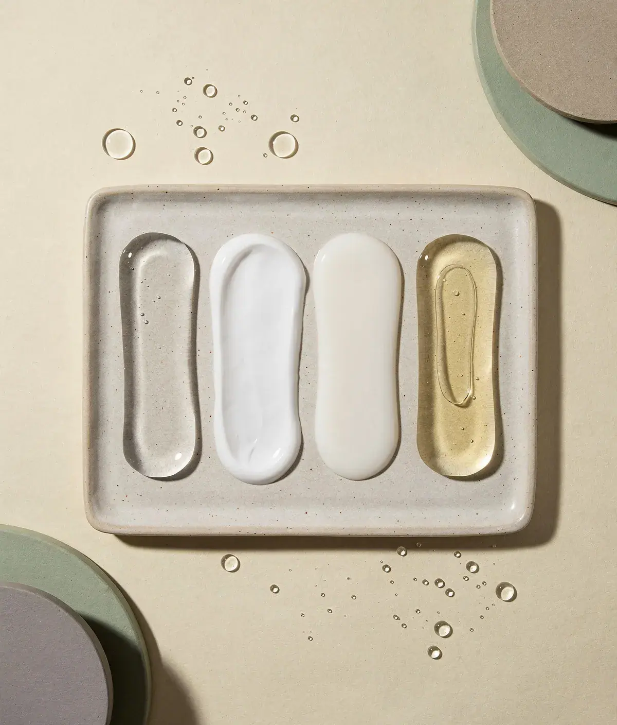 Muestras de gel, loción, body milk y aceite seco sobre una bandeja de cerámica.