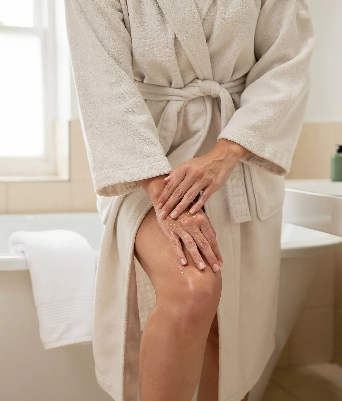 Persona adulta aplicando gel corporal en la pierna con un masaje suave en un baño minimalista.